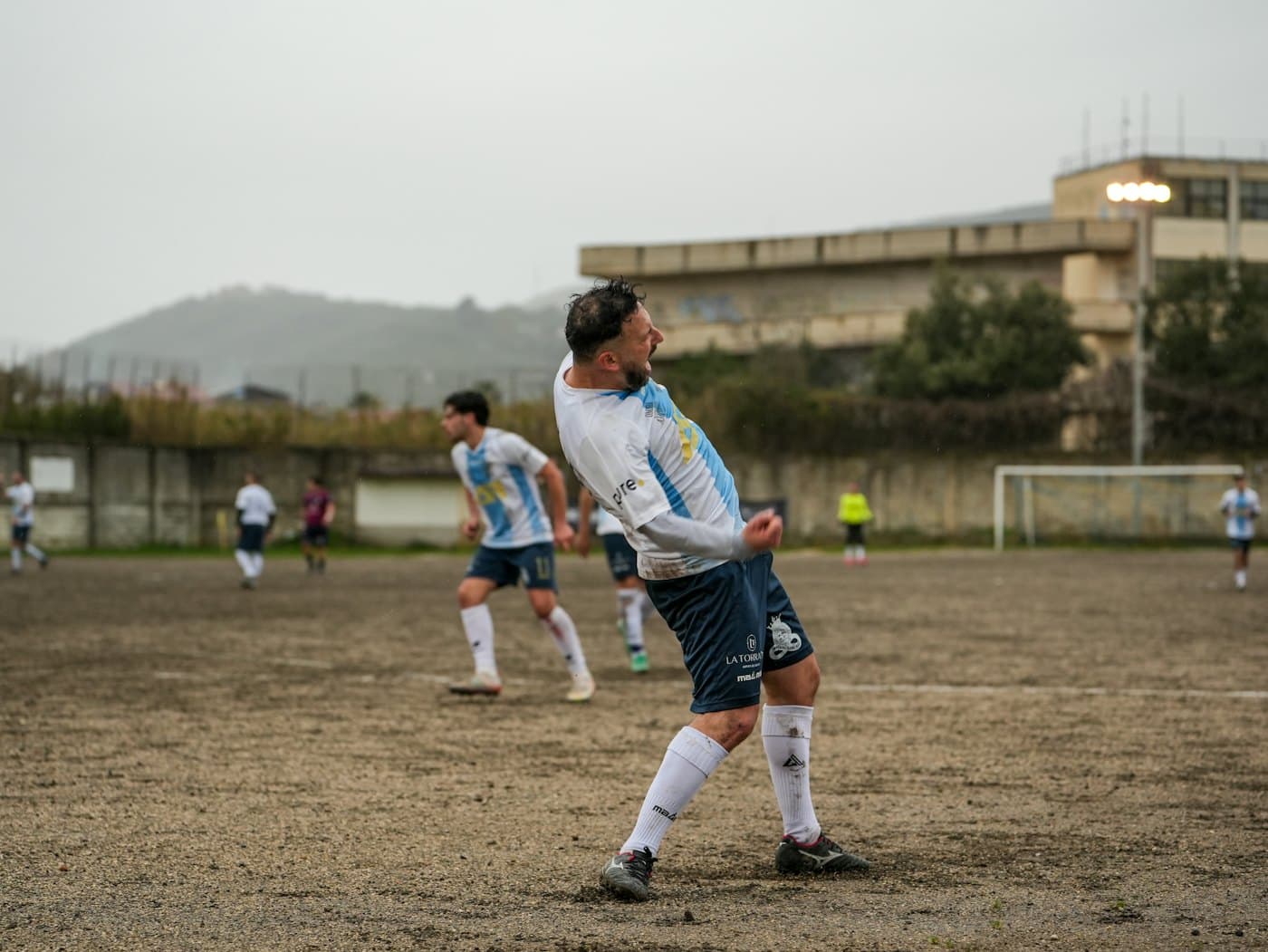 Amateur footballer celebrating on a muddy pitch